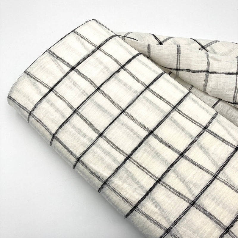 A bolt of white linen fabric with a black windowpane design laying on a white background.